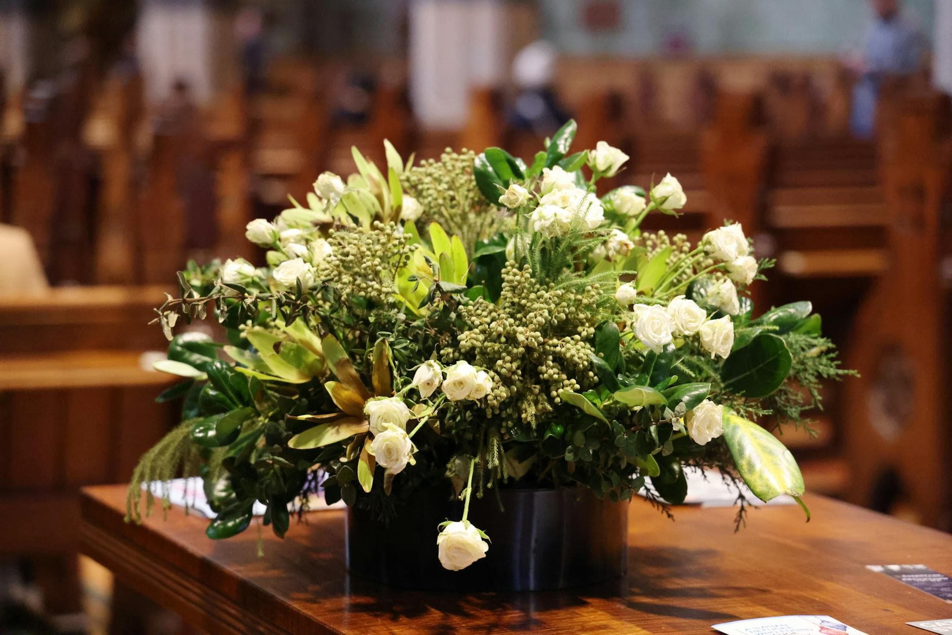 White rose memorial floral arrangement on church pew